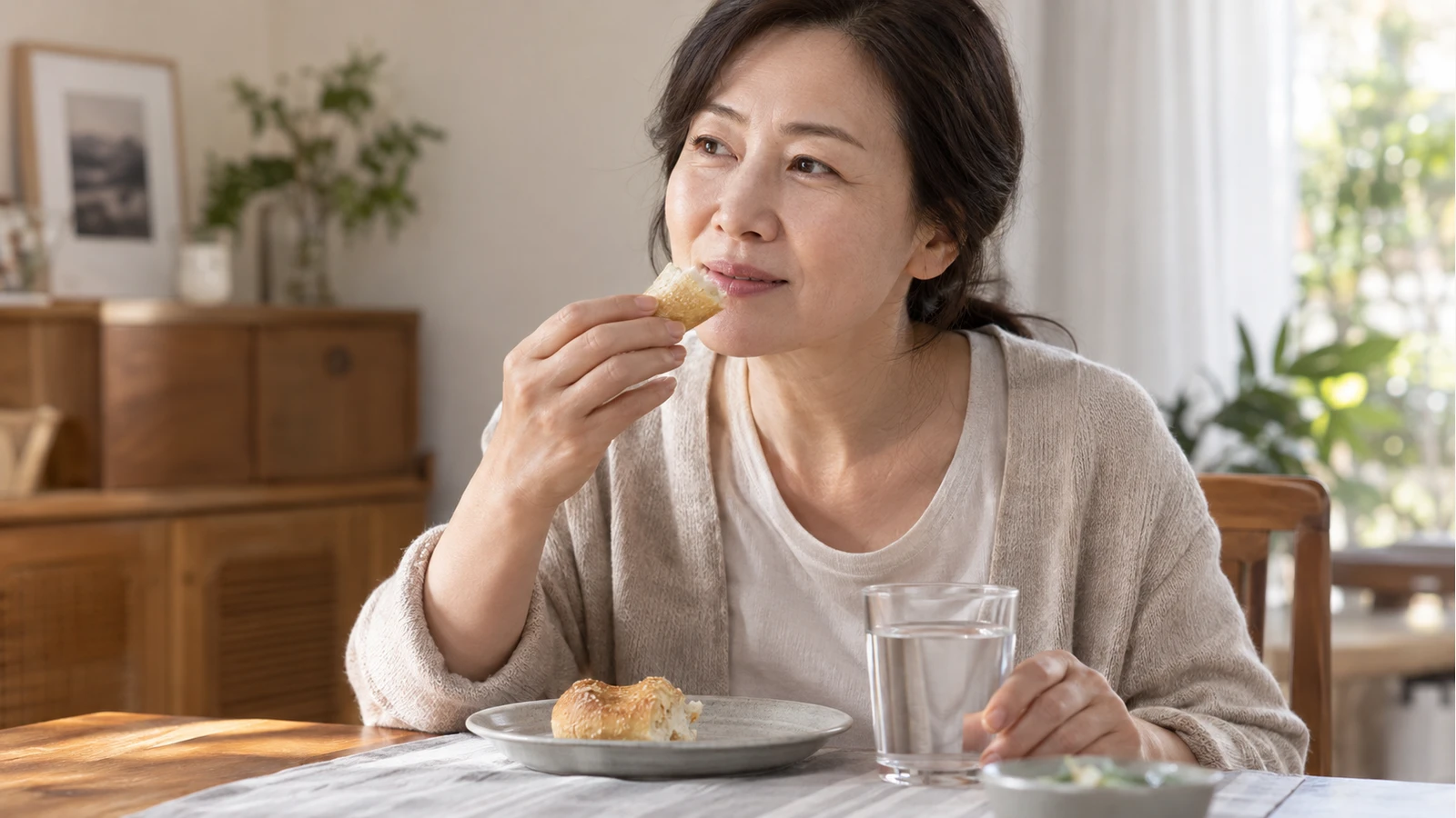빵 조각을 입 가까이 든 여성이 다른 손으로 식탁 위 물컵을 잡고 있는 모습