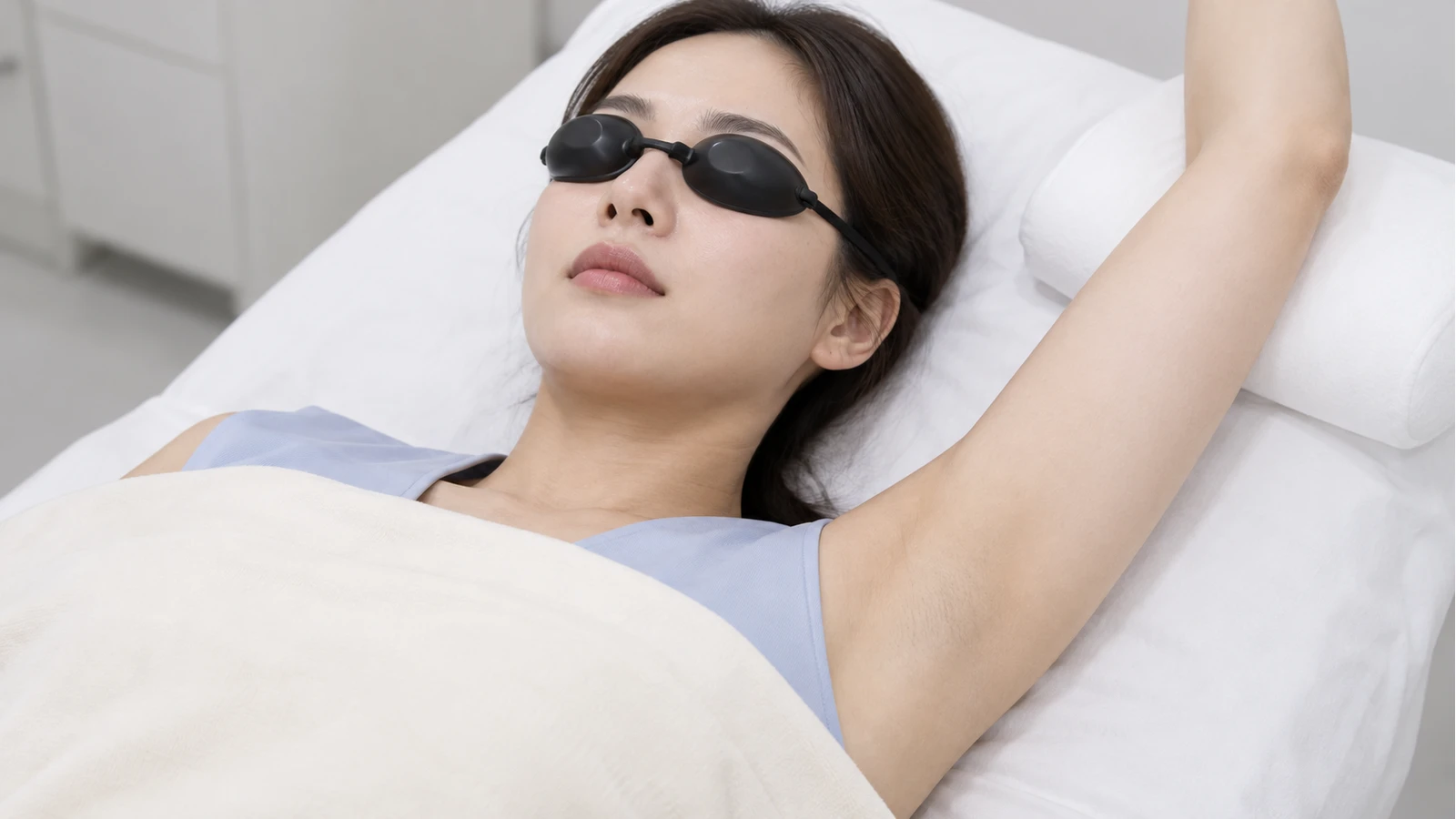 불투명 눈 보호구를 쓴 성인이 진료 침대에 누워 한 팔을 흰 받침에 지지한 겨드랑이 시술 준비 모습