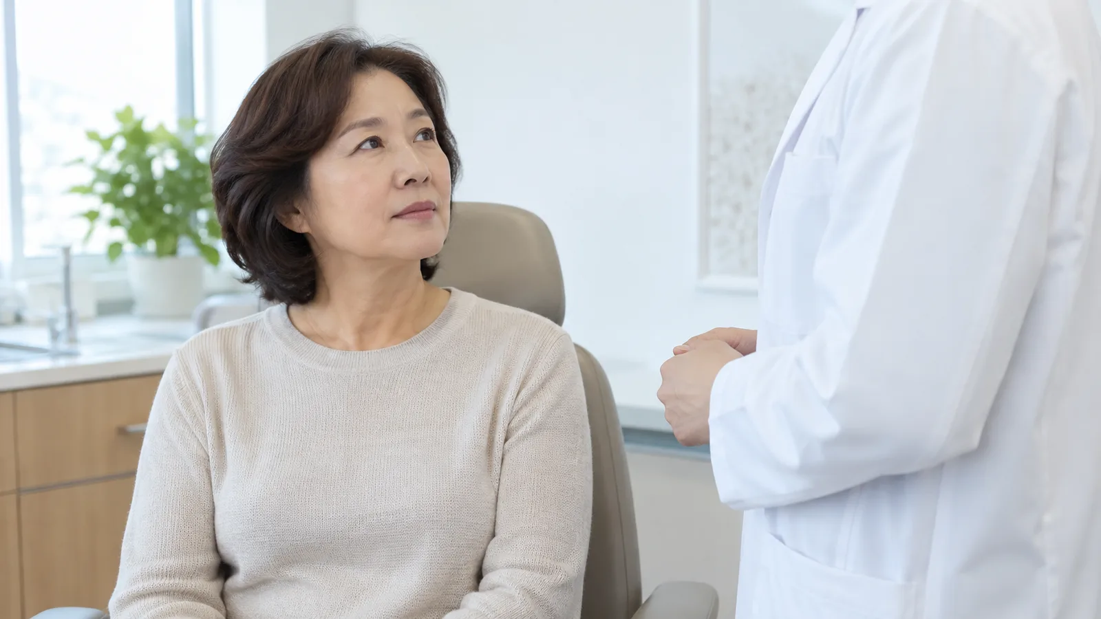 밝은 진료실 의자에 앉은 50대 여성이 옆에 선 흰 가운 차림 의료진을 올려다보며 이야기를 듣고 있다.